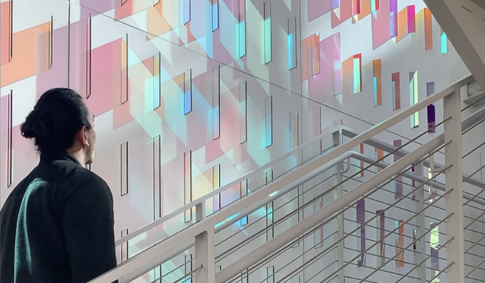 Woman walking up staircase beside a wall of diachroic color glass